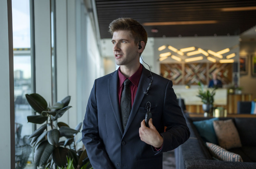 Hotel staff member wearing a Motorola TLK 25 radio on a badge clip with an earpiece in a hotel lobby.